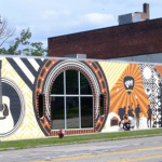 Custom mural being painted on the face of the Elderly Instruments building in Lansing, MI